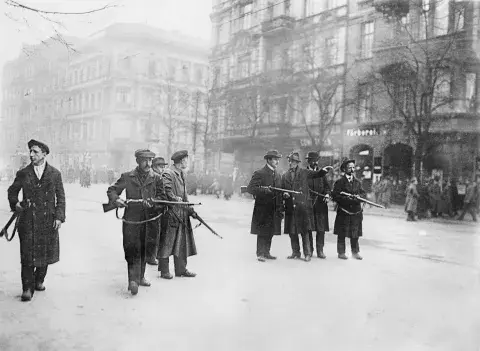 A line of armed revolutionaries of the Spartacist Movement standing in a Berlin street.
