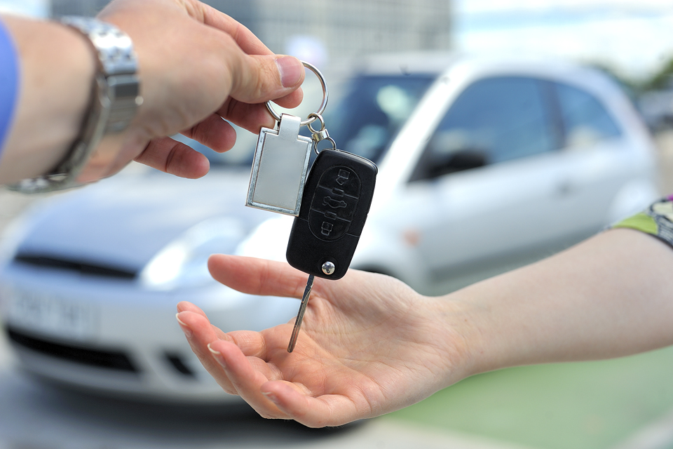 car key being passed from one hand to another in front of a silver car