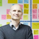 Headshot of Ash Stephens standing in front of a wall with multicoloured postits on