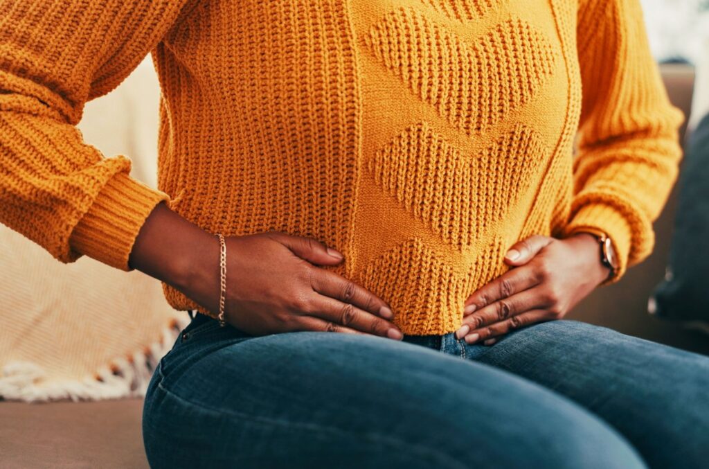 A seated woman wearing an orange jumper holds her stomach