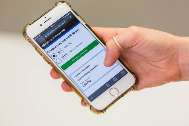 A user using a mobile phone showing GOV.UK Pay payment options on screen.