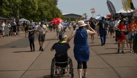 A a person in a wheelchair is being pushed by someone at a busy air show ground