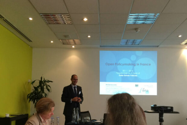 Picture of Romain Lacombe speaking at the front of a conference room, in front of a slide titled 'Open Policymaking in France'