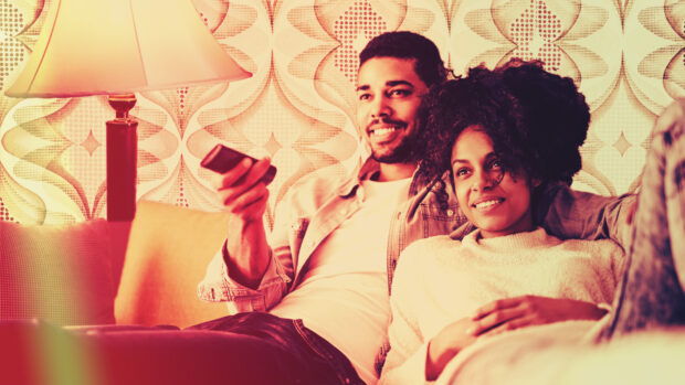 Front view of couple sat on sofa with TV remote