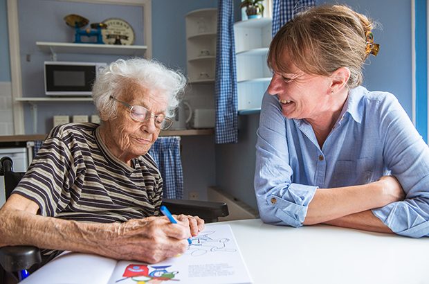 A woman sat with an elderly lady colouring a picture.