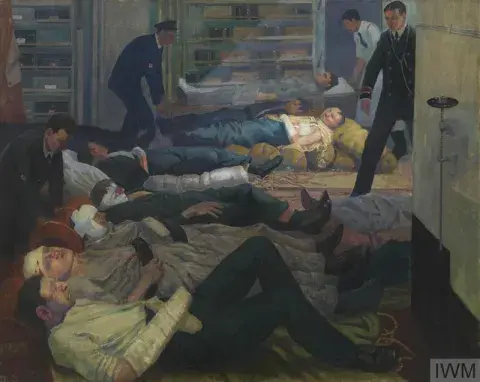 Cabin below deck with several wounded sailors, most swathed in bandages, laid out parallel to one another across the floor. 