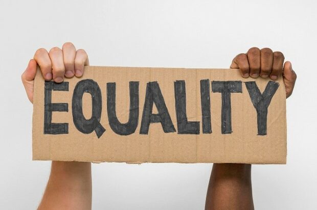Black and white hands holding up a sign with the word 'equality'.