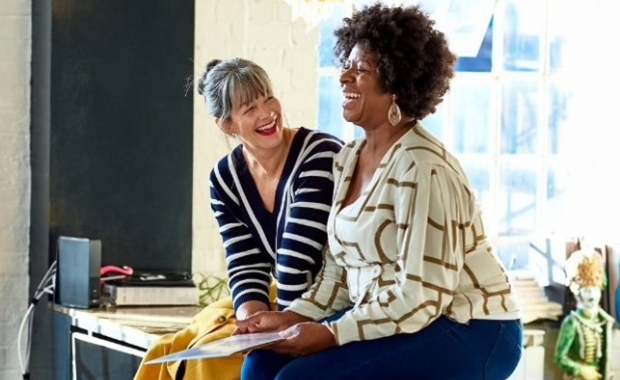 2 ladies sat on a desk laughing