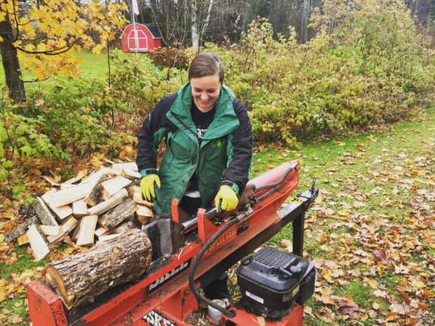 A woman smiling wearing a green coat using a log splitter