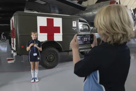 Two school children on gallery in the American Air Museum. One girl is performing with a microphone, whilst the other records her on a mobile phone.