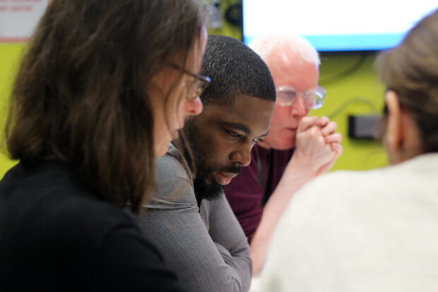 Closeup of two women and men in a workshop at GDS, looking at something in front of them
