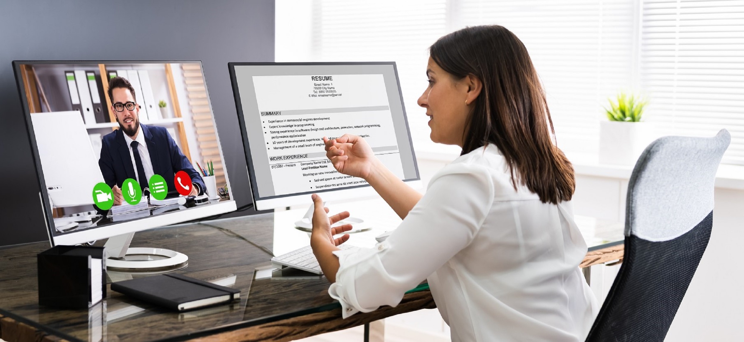 Woman interviewing a man on one screen and she has his CV open on a second screen.