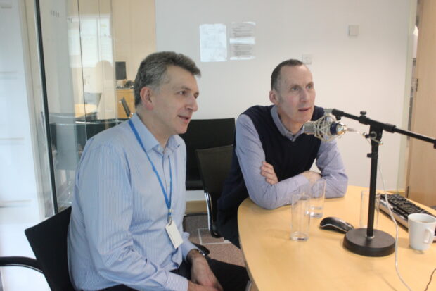 Two men sitting at a desk being videoed for a webinar session