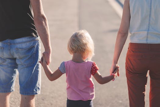Toddler holding the hands of two adults