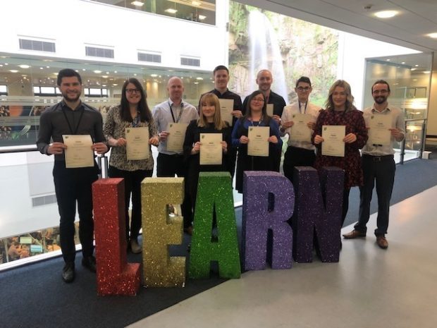 A group of people standing behind a set of letters that spell learn