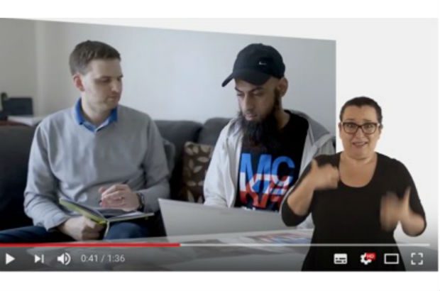 A video still showing a participant being interviewed at home. A signer translates the narration into sign language.