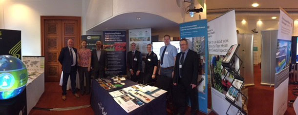 Group of five gentlemen and two women standing at a table containing leaflets with pull-up banners behind them.