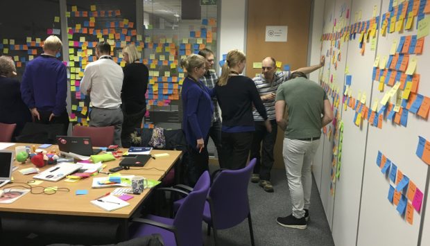 A team crowded round a wall of Post It notes