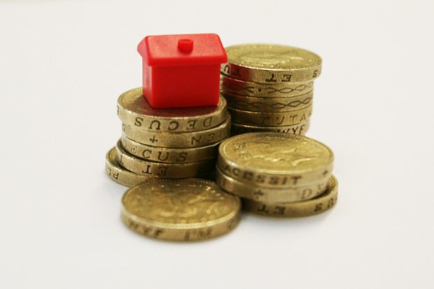 A model house sitting on a pile of coins.