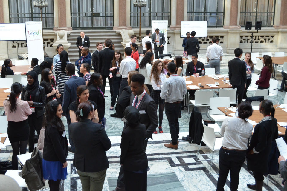 Group of people milling in large marble-floored hall with tables and chairs