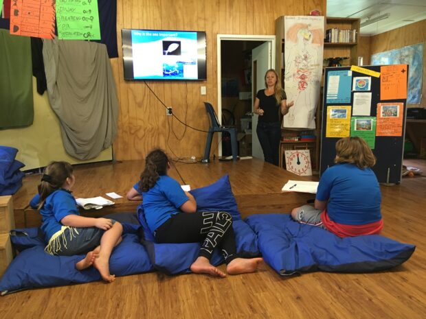 Dr Emily Hardman standing at the front of a classroom as three children look on.