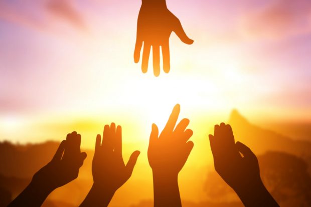 Hands reaching out to each other, with bright sunshine in the background.