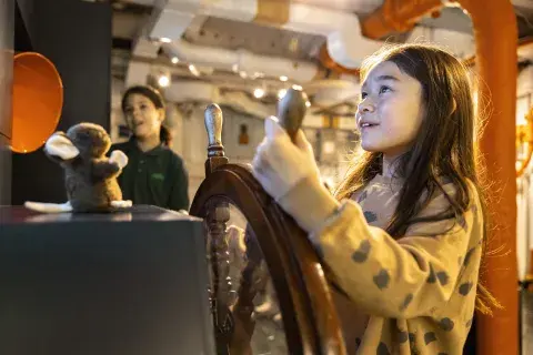 A young girl "steers" HMS Belfast, moving the ship's wheel.