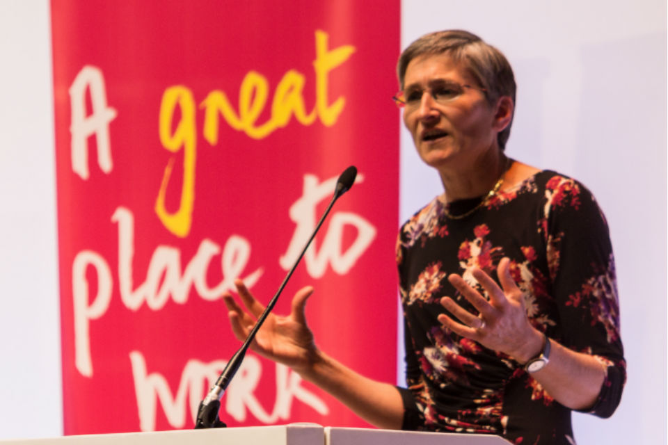 Woman speaking at lectern with banner behind with legend 'A great place to work'