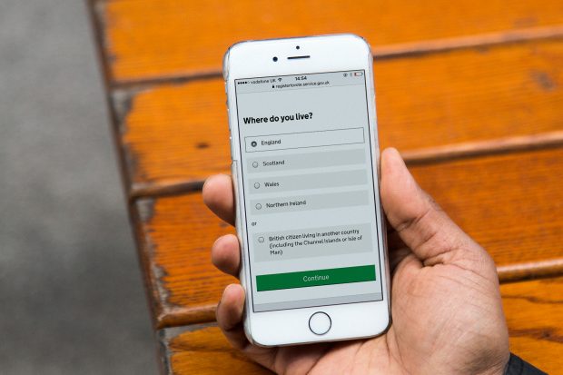 Hand holding mobile phone showing a page on Register to Vote service collecting information about where do you live.