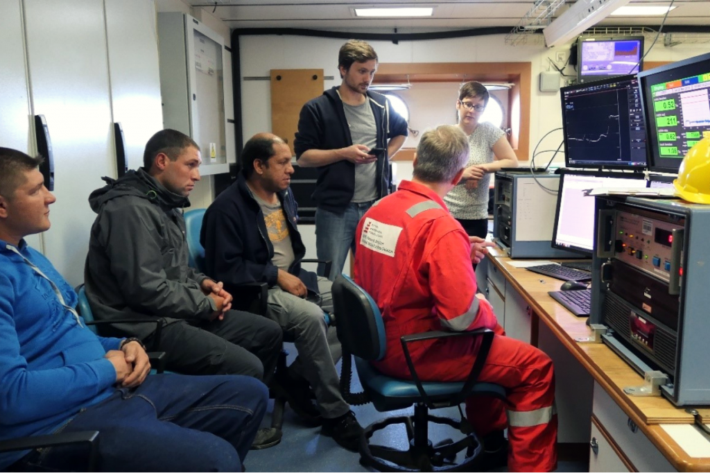 a group of people sitting around monitors and scientific equipment