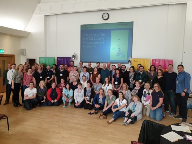 all the delegates, facilitators and project team standing in staggered rows in front of a screen which says "Welcome to the first CS Local NI Future Leaders Academy".