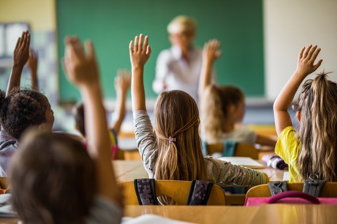 students holding hands up to answer teachers question