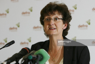 Image of a lady in a black jacket speaking into a set of microphones.
