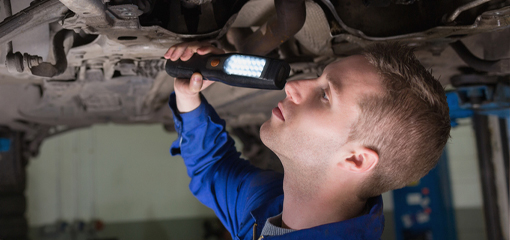 Tester looking underneath car with torch