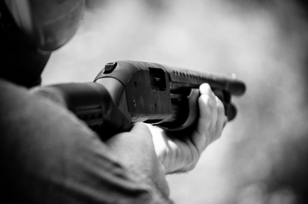 Close-up black and white image of someone holding a shotgun at a firing range