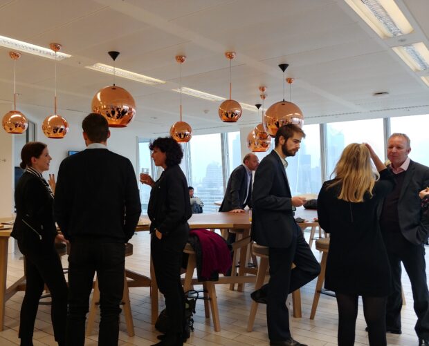 6 smartly dressed people are chatting in two groups of three. In the backdrop there are large windows through which one can see the London skyline. The picture was taken at the government innovation workshop at the Shard organised in collaboration with Warwick Business School.