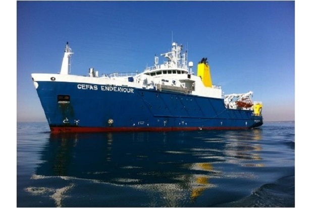 A large fishing vessel, with a blue hull, sitting in calm waters and with a bright blue sky in the background.