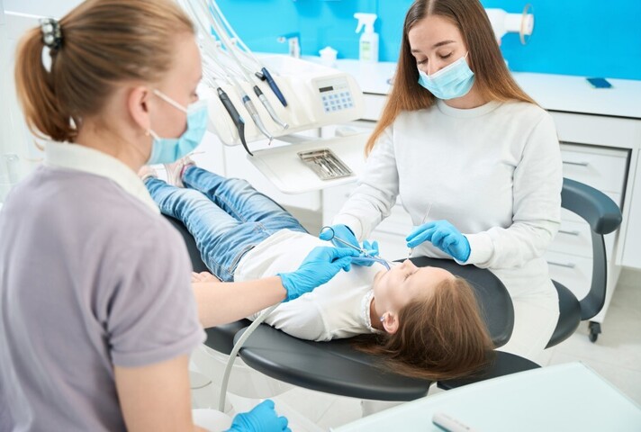 pedodontist giving local anaesthetic injection to girl assisted by nurse