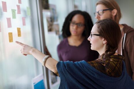Woman leading discussion with two colleagues while pointing at ideas board