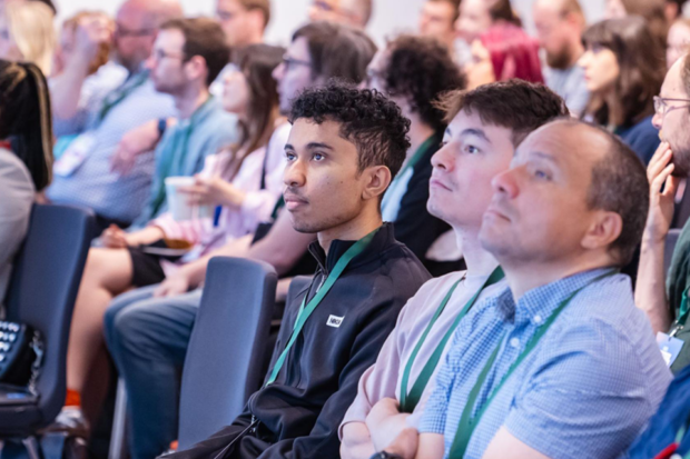 A large group of civil servants sitting in an audience looking up at a screen.