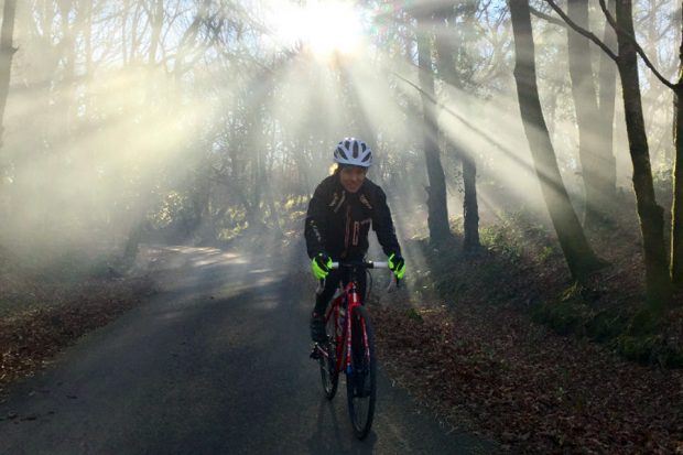 Rachel Jones cycling through woodland, with dappled light through tress