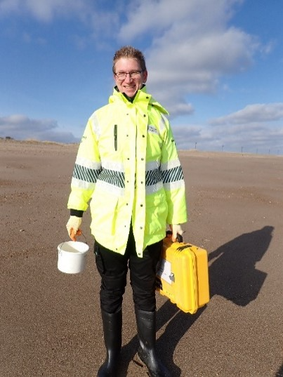 EA Environment Officer standing on a beach with equipment for testing for black algae.