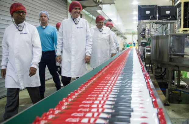 Minister Rutley and several other people walking past a supply chain conveyor belt at the Nestle factory.
