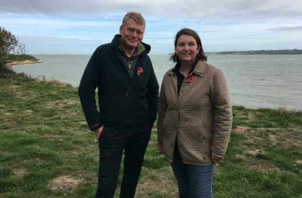 Nicola Spence and Tom Heap stand in a field against a body of water.
