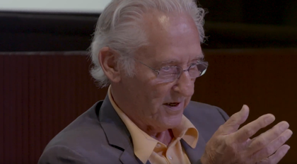 film still of ed ruscha sitting down in a suit and talking in front of a live audience