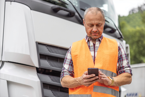 Man in orange high vis in front of a lorry checking his phone