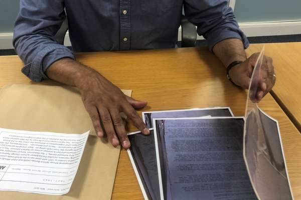 A person sat at a table turns over pages from a historical document beside a brown envelope.