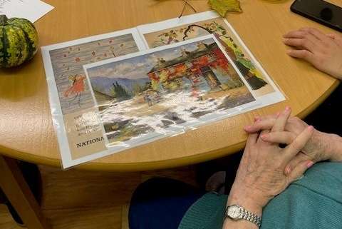 Photo shows the hands of participants discussing Autumnal images on a table decorated with leaves, seasonal vegetables, tea lights and a magnifying glass.