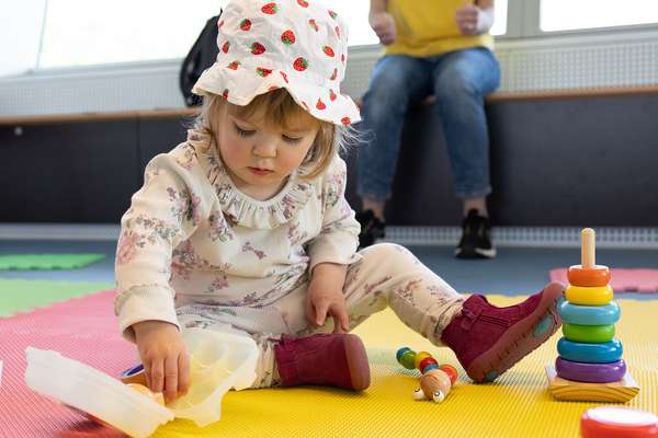 A child presses a colourful shape into a plastic box beside a smiling toy insect.