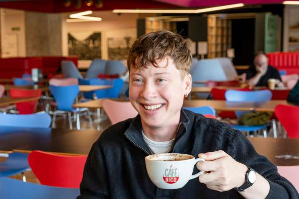 A smiling visitor seated at a table holds a cup of coffee in The National Archives café.